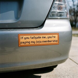 May include: A silver car's bumper with a rectangular bumper sticker. The sticker has a brown background with an orange border and reads, "If you tailgate me, you're paying my Loja membership."