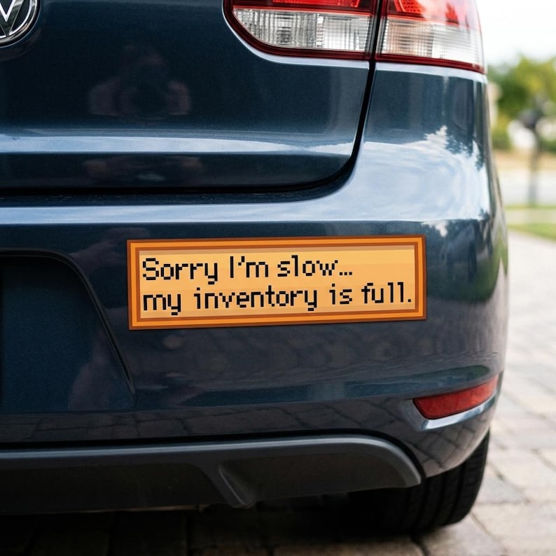 May include: A rectangular bumper sticker with the text "Sorry I'm slow... my inventory is full." The sticker has a pixelated design with a wood-grain background and black text. It is affixed to the rear of a dark blue car.