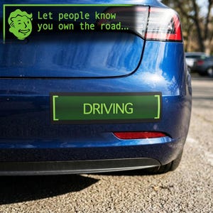 May include: A blue car with a green bumper sticker that says "DRIVING." Above the bumper sticker is a green graphic and the text "Let people know you own the road..." The car is parked on a paved surface.