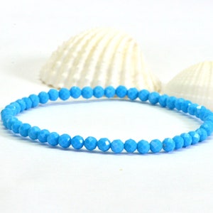 May include: A turquoise blue gemstone bracelet made with faceted beads. The bracelet is on a white background with seashells.