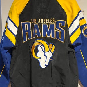 May include: Black, blue, and yellow Los Angeles Rams jacket. The jacket features the team name and logo on the back. The sleeves are blue with yellow and white stripes. The collar and cuffs are blue and white striped.