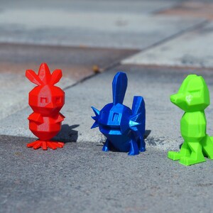 May include: Three 3D printed figurines, each with a different color and design. The first figurine is red and has a bird-like shape. The second figurine is blue and has a fish-like shape. The third figurine is green and has a lizard-like shape.