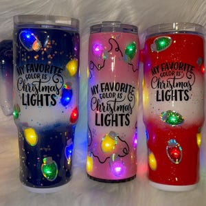 以下が含まれることがあります： 「MY FAVORITE COLOR IS Christmas LIGHTS」の文字とクリスマスライトが付いた、断熱タンブラー3個セット。タンブラーはネイビーブルー、ピンク、レッドで、キラキラとカラフルなLEDライトが付いています。