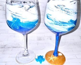 Könnte beinhalten: Zwei Weingläser mit blau-weißen Ozeanwellen-Designs. Der Boden eines Glases ist mit einem goldenen Seestern und einer Muschel verziert.