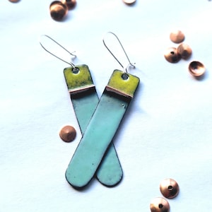 May include: A pair of handmade earrings with a rectangular design. The top section is lime green, transitioning to a dark brown band, and then a light blue body. The earrings have silver-colored ear wires. Small copper-colored embellishments are scattered around.