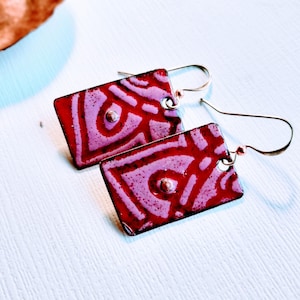May include: A pair of red and white enamel earrings with a geometric pattern. The earrings are rectangular in shape and have a silver bead in the center.