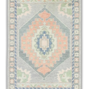 May include: A light blue rug with a geometric pattern in shades of pink, green, and blue. The rug has a border with a repeating pattern.