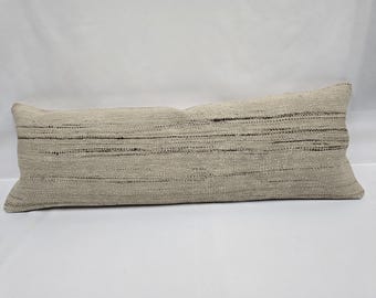 May include: A long, rectangular cushion in neutral tones. The cushion has a woven texture with horizontal dark brown stripes. The cushion is approximately 76 cm long.