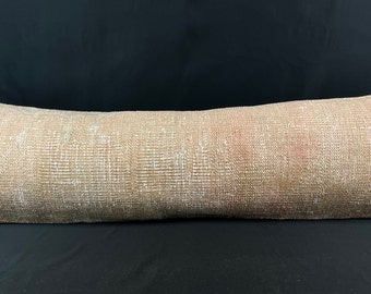 May include: A long, rectangular, beige throw pillow with a woven texture. The pillow has a subtle pink hue and is made of a soft, comfortable fabric.