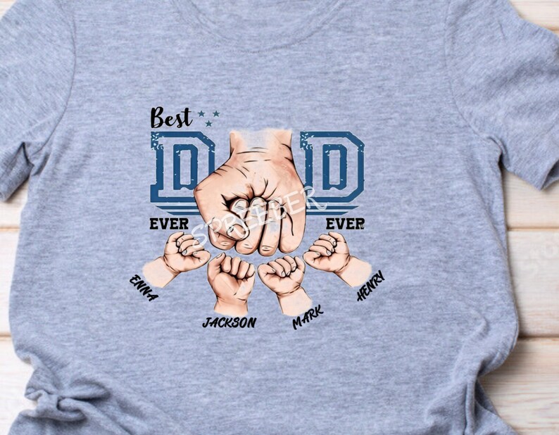 May include: Gray t-shirt with a blue graphic of a fist with the word "DAD" in blue letters and the words "Best Ever" on either side.  The fist is surrounded by four smaller fists with the names "Emma", "Jackson", "Mark", and "Henry" written below.
