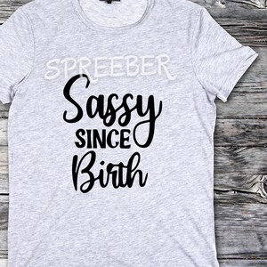 May include: Gray t-shirt with black text that reads "Sassy Since Birth".
