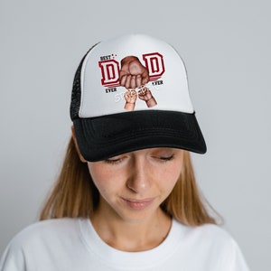 May include: A black and white trucker hat with a red and white graphic that says "Best Dad Ever" with a hand holding a smaller hand.