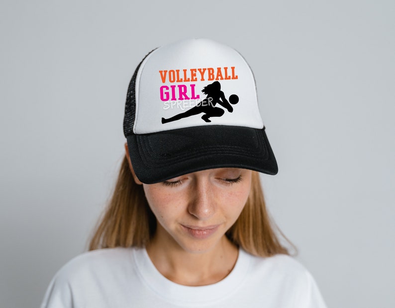May include: A black and white trucker hat with a white front panel. The front panel features a silhouette of a volleyball player with the text "VOLLEYBALL GIRL SPREADER" in orange and pink.