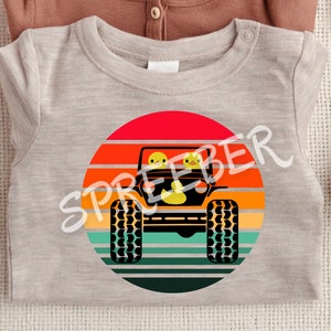 Może przedstawiać: Szary t-shirt z grafiką w stylu retro przedstawiającą jeepa z dwoma ż&oacute;łtymi gumowymi kaczkami w środku, jadącego przez zach&oacute;d słońca.