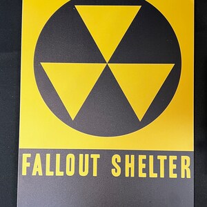 May include: A yellow and black metal sign with a black circle containing a yellow radiation symbol and the text "FALLOUT SHELTER".