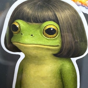 May include: A sticker featuring a cartoon frog with a green body, large yellow eyes, and a brown bob haircut. The frog is smiling and has a white border.