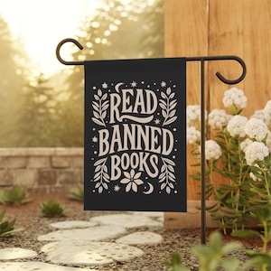 May include: A black garden flag with white text that reads "Read Banned Books". The text is surrounded by a floral design and stars.