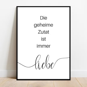 Peut inclure: Une affiche encadrée avec un bord noir présente le texte allemand "Die geheime Zutat ist immer liebe" en script noir. La phrase se traduit par "L'ingrédient secret est toujours l'amour."
