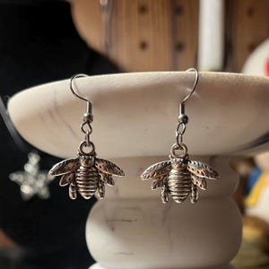 May include: A pair of silver bee dangle earrings. The bees have detailed wings and bodies.