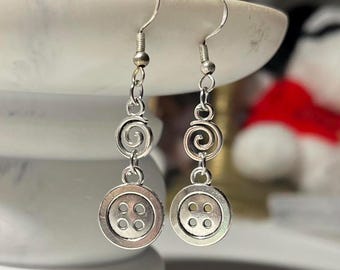 May include: Silver-toned dangle earrings. Each earring features a button charm with four holes, connected to a spiral design and a hook. The earrings are displayed against a blurred background.