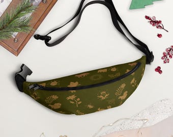 May include: Olive green fanny pack with a black adjustable strap and zipper. The pack is patterned with gold-colored nature-themed illustrations, including flowers, suns, and animals. The bag is designed to be worn around the waist or across the body.