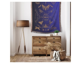 May include: A blue tapestry with a gold design of moths, butterflies, and crescent moons. The tapestry is hanging on a wall above a wooden dresser with drawers.