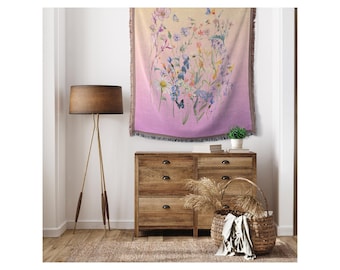 May include: A floral tapestry with a gradient background of light yellow to purple. The tapestry features a variety of colorful flowers and butterflies. It is hanging on a wall above a wooden dresser.