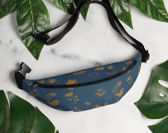 May include: A blue fanny pack with a gold pattern of various nature-inspired designs, including flowers, animals, and the sun. The fanny pack has a black adjustable strap.
