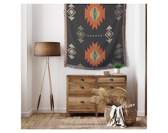 May include: A black and orange geometric patterned throw blanket with fringe hangs on a wall above a wooden dresser with drawers. A wicker basket sits on the floor in front of the dresser.