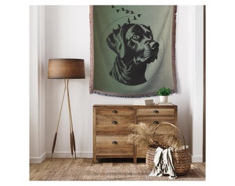 May include: A black and white illustration of a Labrador Retriever's head with birds flying above. The illustration is on a green and brown tapestry with a fringe border.