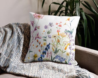 May include: A white throw pillow with a colorful floral pattern. The pillow features a variety of flowers, including pink, blue, yellow, and purple flowers. The pillow is perfect for adding a touch of nature to any room.