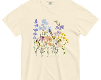 May include: Cream-colored t-shirt featuring a watercolor floral design. The flowers include shades of purple, blue, yellow, and orange. The shirt has a classic crew neck and short sleeves, suitable for casual wear.
