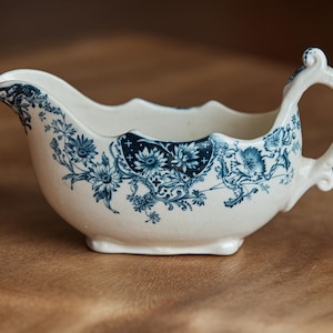 May include: A white porcelain gravy boat with a blue floral design. The boat has a handle and a spout.