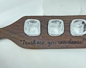 May include: A wooden shot glass tray with four shot glasses. The tray has a handle and is engraved with the text "Trust me, you can dance!" - Tequila.