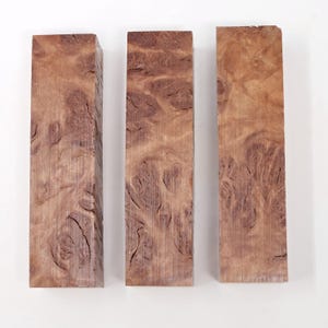 Op de afbeelding: Drie houten blanco's voor het maken van ambachten, elk met een uniek bruin en wit burl-patroon. De blanco's zijn ongeveer 12,7 cm lang en 2,5 cm breed.