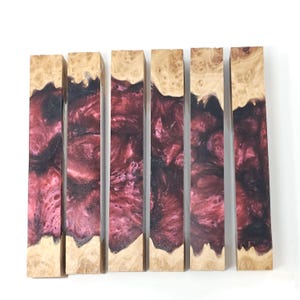 May include: Six rectangular turning blanks arranged vertically, each featuring a combination of natural light-colored burl wood and a deep, swirling magenta and black resin. The wood grain is visible at the top and bottom of each piece.