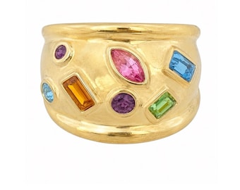 May include: A wide gold band ring featuring a scattered arrangement of multi-colored gemstones. The stones include a marquise-cut pink gem, rectangular-cut blue, orange, and green gems, and round-cut purple and light blue gems set into the metal.
