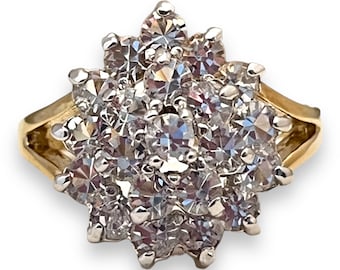 Op de afbeelding: Een gouden ring met een cluster van kleine, heldere diamanten, gezet in een bloemvorm.