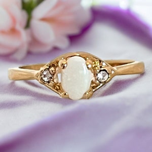 May include: A gold ring featuring a white oval-shaped opal gemstone with two smaller clear gemstones on either side.