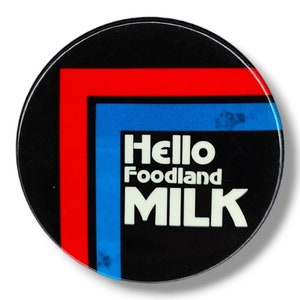 Peut inclure: Un bouton rond noir avec le texte "Hello Foodland MILK" en blanc. Le bouton a un design d'angle rouge et bleu. Il s'agit d'un article vintage.
