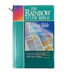 May include: A teal-colored "The Rainbow Study Bible" book with the words "Living Bible Edition" on the cover. The book is color-coded and has bold letters. The cover features an open book with colorful pages.