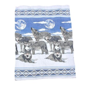 May include: A rectangular towel with a design of gray wolves under a full moon. The background is blue with clouds. The wolves are in various poses, some howling. The top and bottom borders have a geometric pattern in blue and gray.