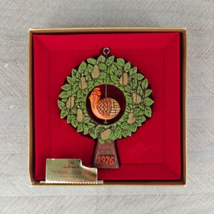 以下が含まれることがあります： 1976年製のヴィンテージHallmarkクリスマスオーナメント。緑色のリースに洋梨とオレンジ色の鳥が中央に描かれています。赤いベルベットの裏地が付いた箱に入っています。オーナメントには「Twirl Abouts」と書かれた金のタグが付いています。