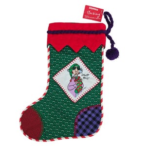 May include: A Christmas stocking with a green patterned body, red top, and a red and white striped border. It features a cartoon image of a person holding a stocking and the text "Stuff this!". A purple pom-pom and tag that says "Shoebox Stocking" are attached.