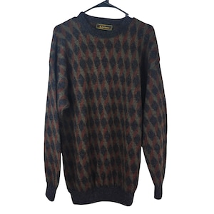 May include: A long-sleeve crew neck sweater featuring a repeating diamond argyle pattern in shades of dark charcoal, muted olive green, and deep rust red. The garment has a ribbed hem and cuffs, and a small rectangular label inside the collar.