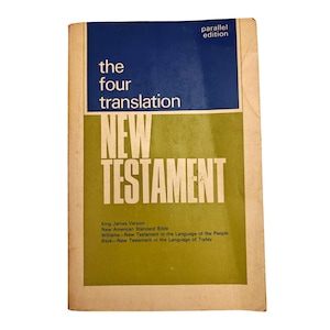 Puede incluir: Un libro de bolsillo vintage titulado "New Testament" con una cubierta azul y verde. La portada dice "the four translation" y enumera diferentes versiones, incluida King James. El libro tiene una apariencia desgastada y envejecida.