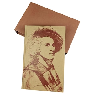 May include: A hardback book with a brown illustration of a man in a hat on the cover, with a matching brown box. The book's cover has a sepia-toned portrait of a man in a hat. The box is open, revealing the book.