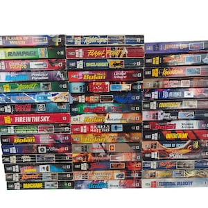 May include: A collection of Mack Bolan paperback books arranged in three vertical stacks. The spines feature various titles including Flames of Wrath, Rampage, Code of Bushido, Predator Paradise, Assault, Deception, Fire in the Sky, and Terminal Velocity.