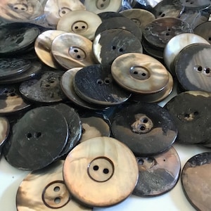 May include: A large pile of brown and black shell buttons with two holes each. The buttons are round and have a smooth, shiny finish.