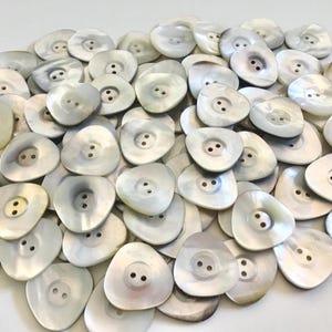 May include: A collection of pearlescent, irregularly shaped buttons with two holes each. The buttons have a slightly iridescent sheen and a smooth, rounded surface. These buttons are ideal for sewing and craft projects.